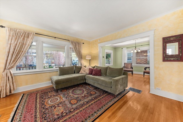 living room featuring wood finished floors, a chandelier, baseboards, ornamental molding, and visible vents