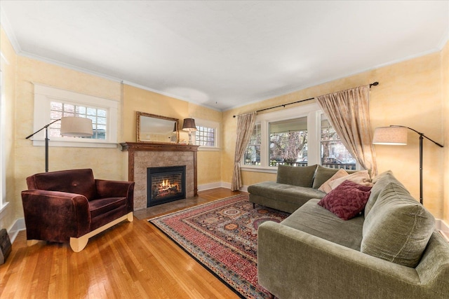 living room featuring baseboards, a tiled fireplace, wood finished floors, and crown molding