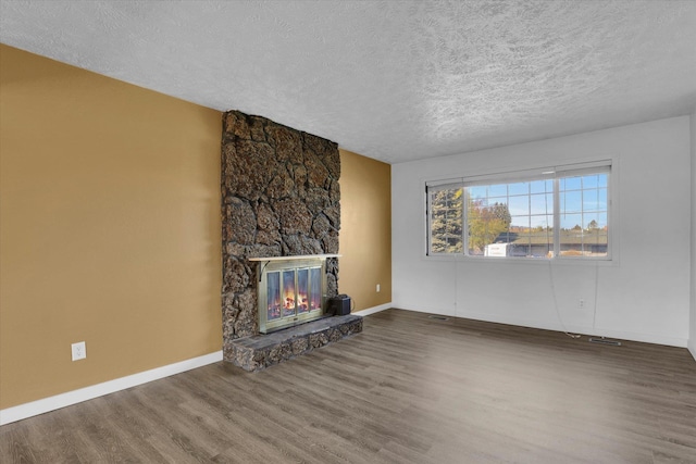 unfurnished living room featuring baseboards, a stone fireplace, wood finished floors, and a textured ceiling
