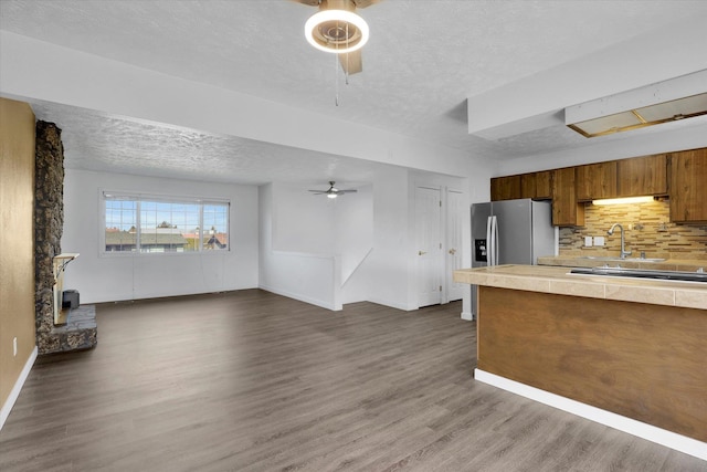 kitchen featuring stainless steel fridge with ice dispenser, a wood stove, a ceiling fan, dark wood-type flooring, and a textured ceiling