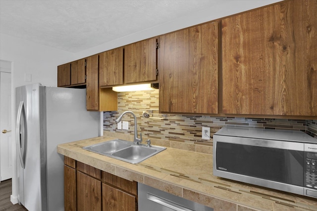 kitchen with brown cabinets, stainless steel appliances, backsplash, light countertops, and a sink