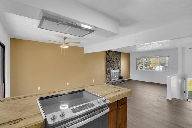 kitchen with dark wood-style floors, a stone fireplace, stainless steel electric stove, open floor plan, and ceiling fan