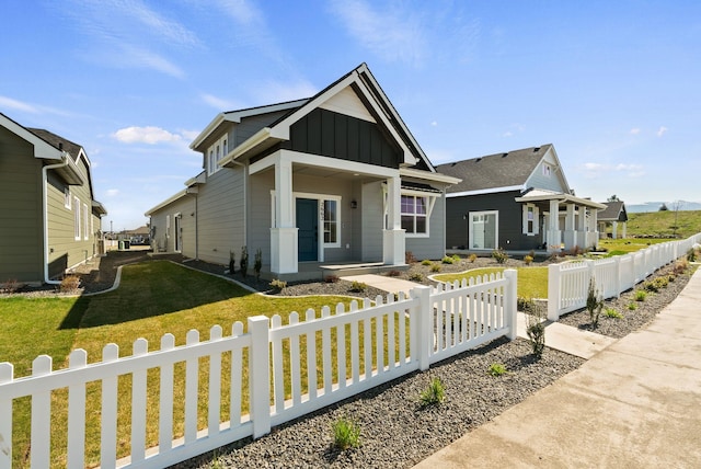 view of front of property with a front lawn, covered porch, board and batten siding, and a fenced front yard