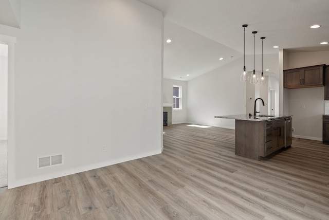kitchen with a sink, open floor plan, a glass covered fireplace, lofted ceiling, and visible vents
