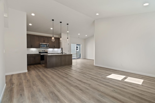 kitchen featuring stainless steel appliances, dark brown cabinets, open floor plan, backsplash, and an island with sink