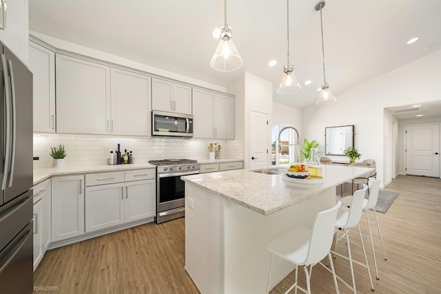 kitchen with light stone counters, light wood-type flooring, decorative light fixtures, decorative backsplash, and appliances with stainless steel finishes