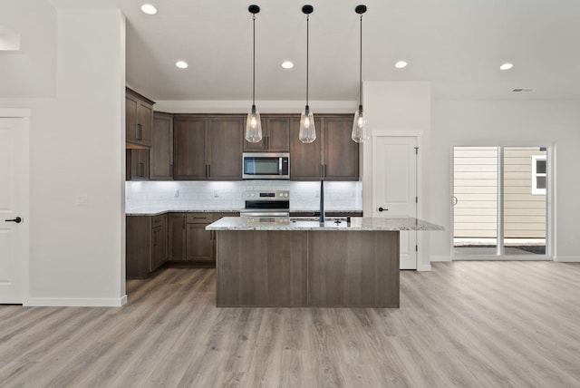 kitchen featuring tasteful backsplash, an island with sink, light wood-style floors, appliances with stainless steel finishes, and light stone countertops