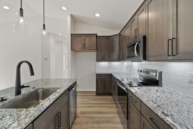 kitchen featuring a sink, light wood-style floors, backsplash, lofted ceiling, and appliances with stainless steel finishes