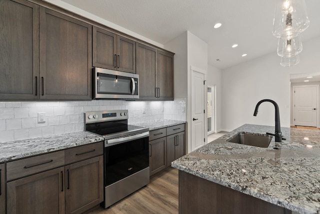 kitchen with a sink, light wood-type flooring, dark brown cabinetry, decorative backsplash, and appliances with stainless steel finishes