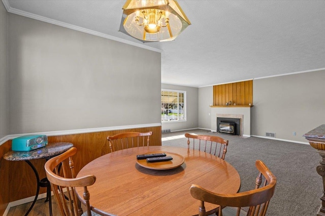 carpeted dining area featuring a textured ceiling, a fireplace with flush hearth, baseboards, ornamental molding, and visible vents