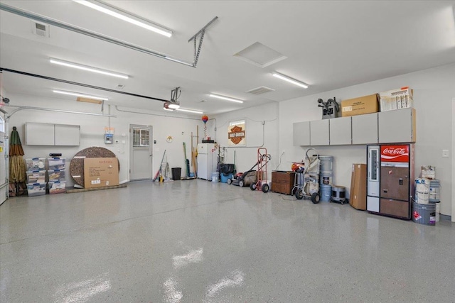 garage featuring a garage door opener, visible vents, and freestanding refrigerator