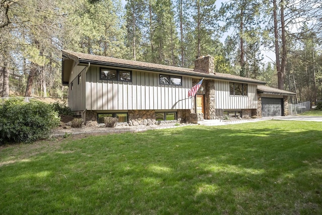 bi-level home featuring a chimney, a front lawn, an attached garage, board and batten siding, and driveway