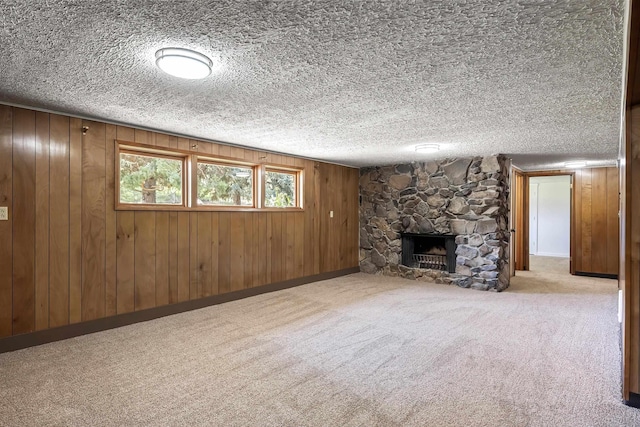 unfurnished living room with wood walls, a stone fireplace, carpet floors, baseboards, and a textured ceiling