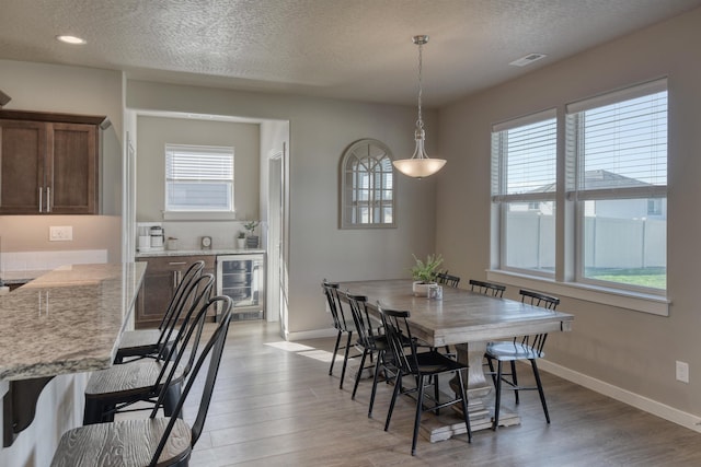 dining area featuring light wood-type flooring, visible vents, beverage cooler, and a healthy amount of sunlight