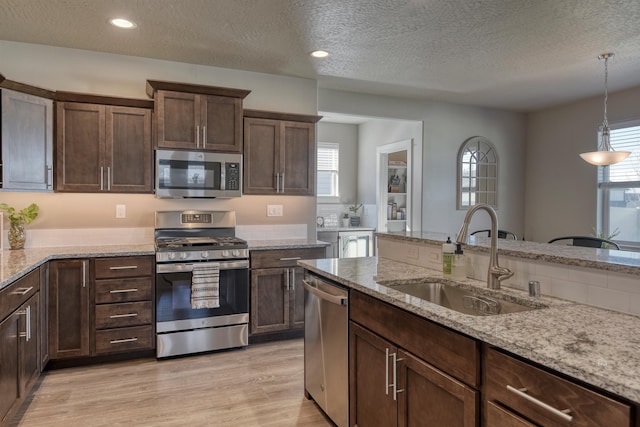 kitchen featuring a textured ceiling, a sink, stainless steel appliances, light wood-style flooring, and decorative light fixtures