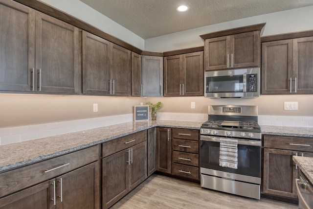 kitchen with dark brown cabinets, light wood-type flooring, a textured ceiling, and stainless steel appliances