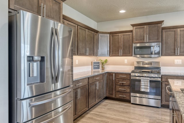 kitchen with light wood-style flooring, a textured ceiling, recessed lighting, light stone countertops, and appliances with stainless steel finishes