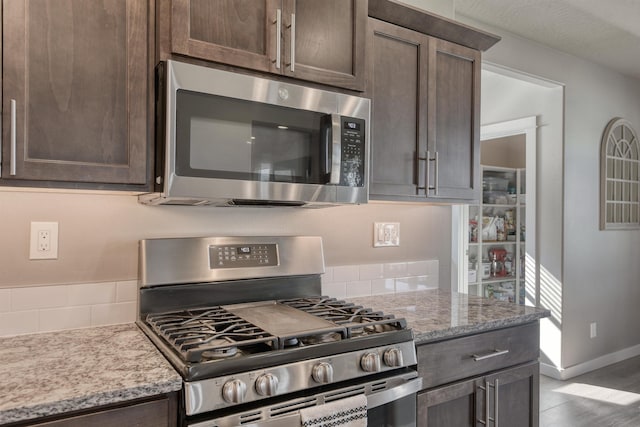 kitchen featuring light stone countertops, stainless steel appliances, dark brown cabinetry, and backsplash