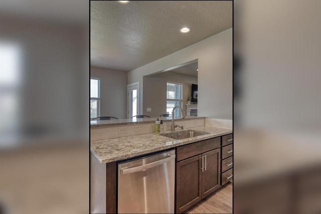 kitchen featuring stainless steel dishwasher, a sink, a textured ceiling, light wood-style floors, and light stone counters