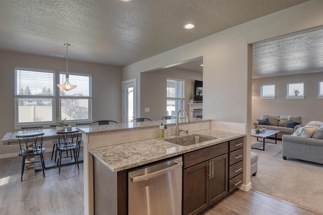 kitchen with stainless steel dishwasher, a sink, light wood-style floors, a textured ceiling, and open floor plan