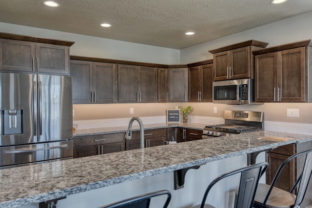 kitchen featuring a textured ceiling, light stone countertops, appliances with stainless steel finishes, and dark brown cabinetry