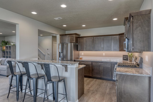 kitchen featuring light stone countertops, stainless steel appliances, light wood-style flooring, and a textured ceiling