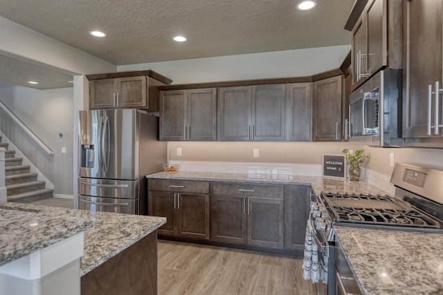 kitchen featuring a textured ceiling, appliances with stainless steel finishes, dark brown cabinetry, and light stone counters