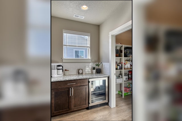 bar with wine cooler, a textured ceiling, visible vents, light wood-style floors, and decorative backsplash