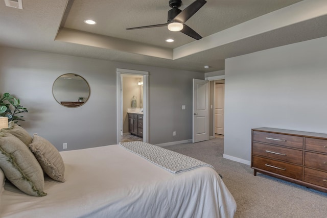 bedroom with a tray ceiling, visible vents, light carpet, connected bathroom, and baseboards