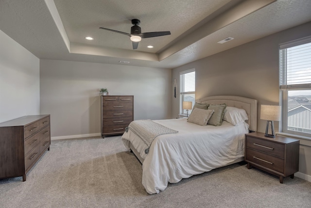 bedroom featuring a tray ceiling, visible vents, baseboards, and light carpet