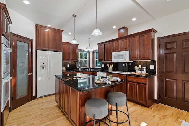 kitchen featuring a center island, light wood-type flooring, backsplash, white appliances, and decorative light fixtures