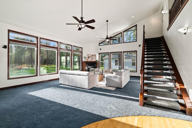 carpeted living area featuring stairway, ceiling fan, baseboards, and high vaulted ceiling