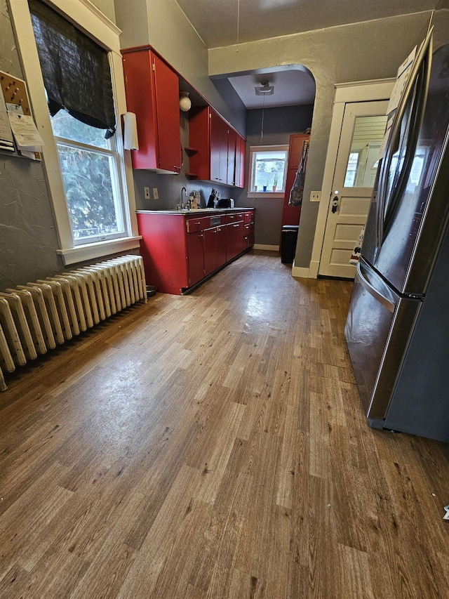 303 N Vernon St, Deer Park, WA 99006 - kitchen featuring radiator heating unit, red cabinets, wood finished floors, arched walkways, and freestanding refrigerator