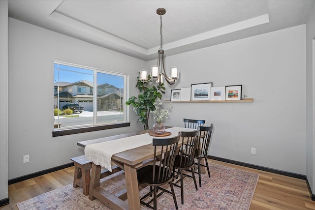 dining area with baseboards, wood finished floors, a tray ceiling, and an inviting chandelier