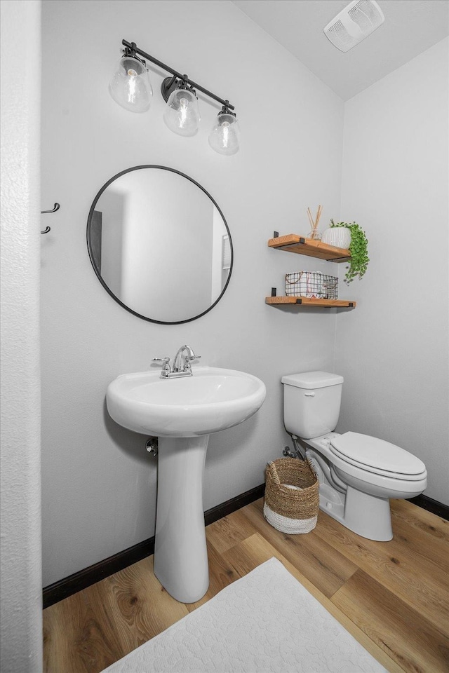 half bath with wood finished floors, visible vents, toilet, and baseboards
