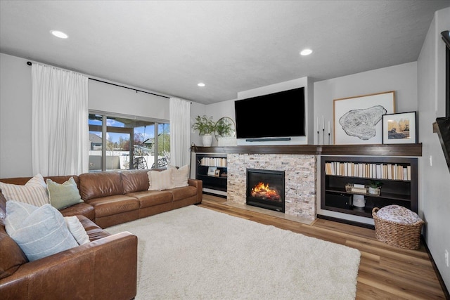 living area featuring a fireplace with flush hearth, wood finished floors, and recessed lighting