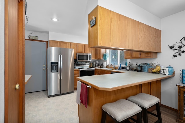 kitchen with light countertops, a sink, a peninsula, brown cabinetry, and appliances with stainless steel finishes