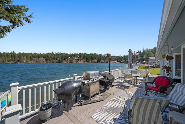wooden terrace featuring a grill, a forest view, outdoor dining space, and a water view