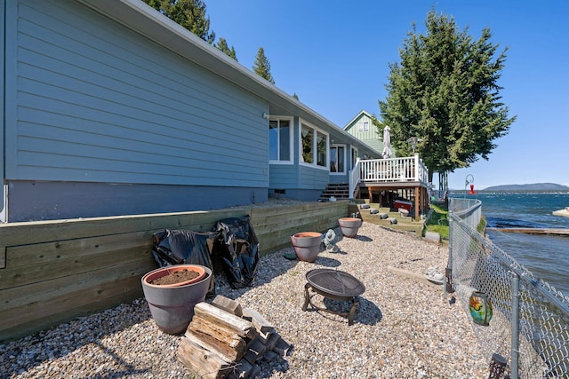 view of side of property featuring a deck with water view, stairs, fence, crawl space, and an outdoor fire pit