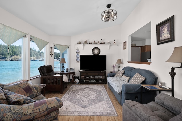 living area featuring lofted ceiling, an inviting chandelier, wood finished floors, and a water view