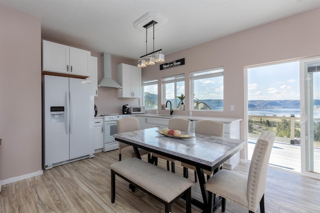 kitchen featuring hanging light fixtures, a sink, white appliances, white cabinets, and wall chimney exhaust hood