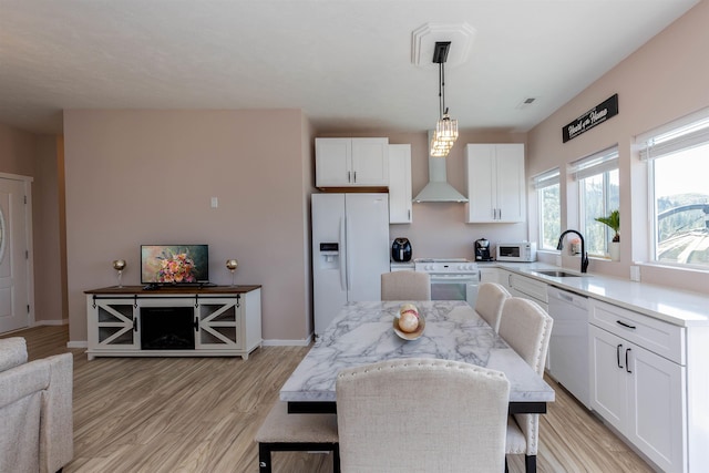 kitchen with wall chimney range hood, a sink, white appliances, light wood-type flooring, and white cabinetry