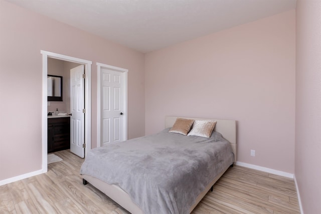 bedroom with connected bathroom, baseboards, and light wood-style flooring