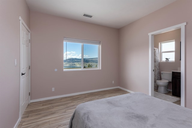 bedroom with connected bathroom, multiple windows, visible vents, and light wood-type flooring