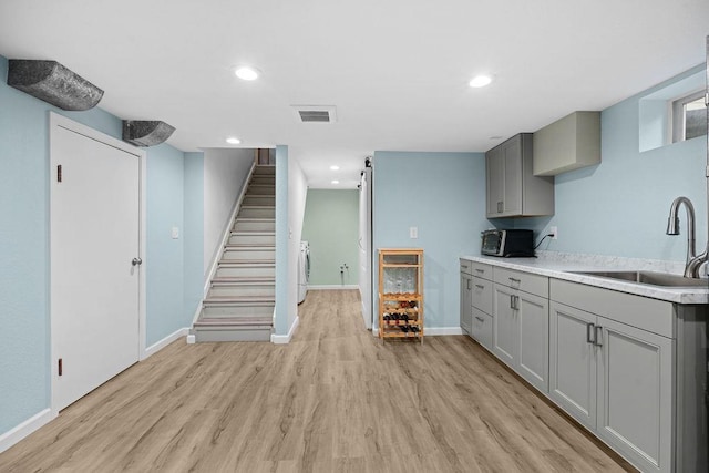 kitchen featuring gray cabinets, a sink, visible vents, and light wood-type flooring