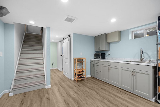 kitchen with a barn door, a sink, light wood-style floors, baseboards, and gray cabinetry