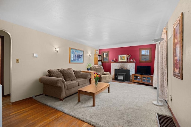 living room featuring a fireplace with flush hearth, arched walkways, baseboards, visible vents, and wood finished floors