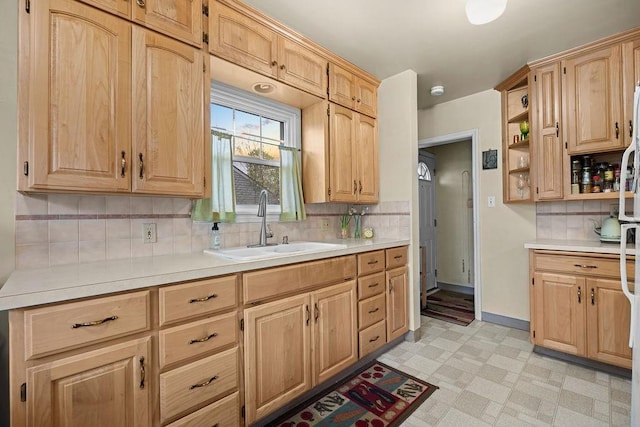 kitchen featuring light countertops, a sink, backsplash, light floors, and light brown cabinets