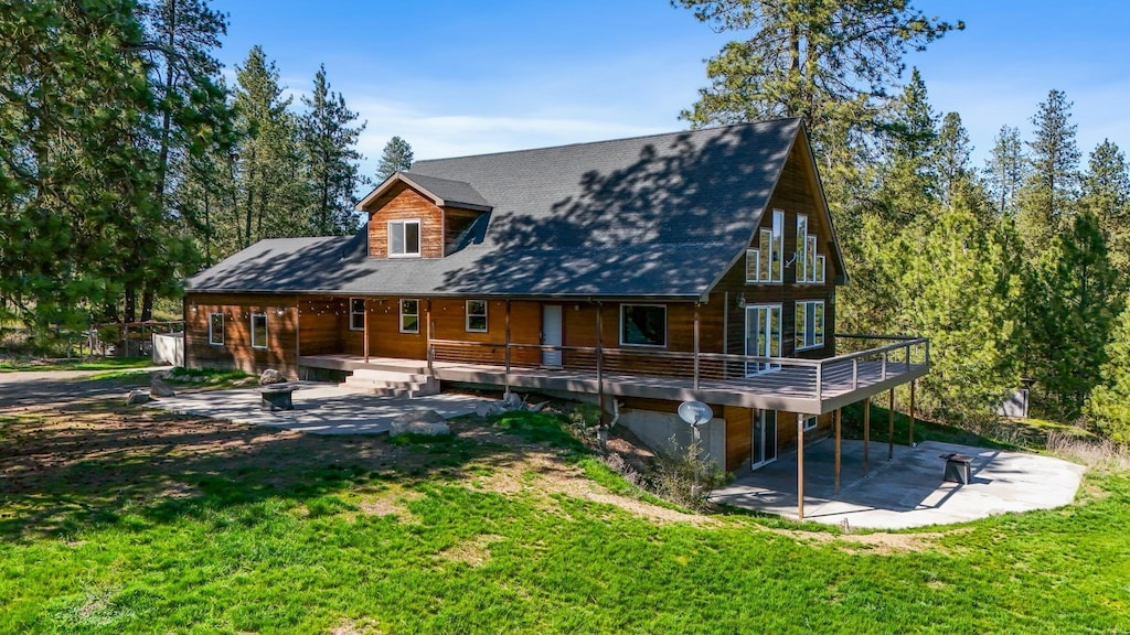 back of property featuring a lawn, a wooden deck, and a patio