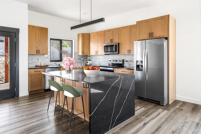 kitchen featuring decorative backsplash, appliances with stainless steel finishes, dark countertops, a kitchen island, and wood finished floors